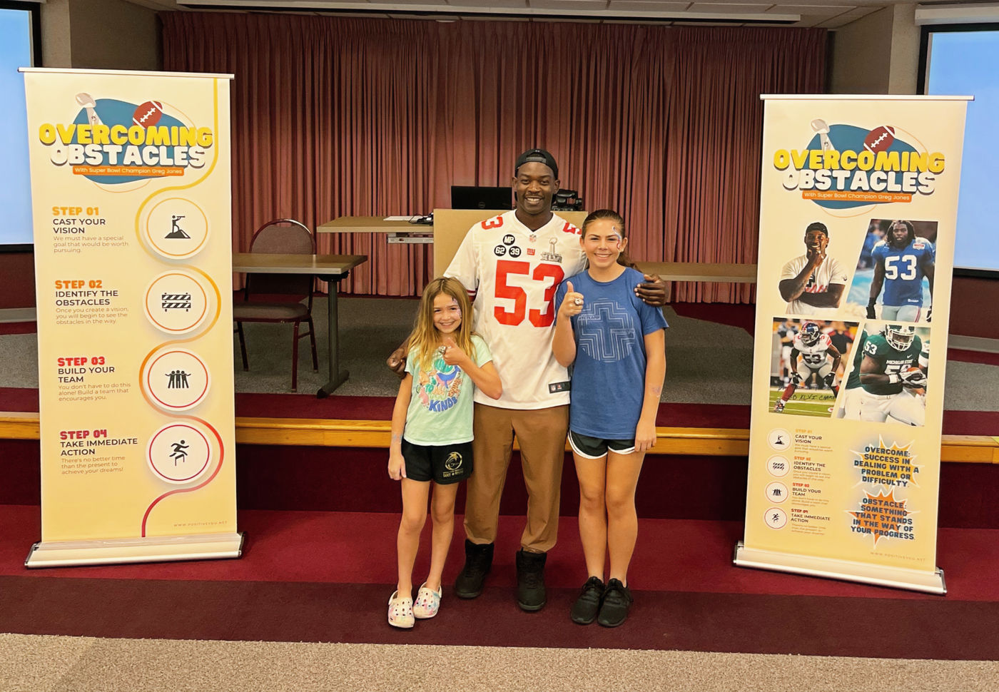A speaker with two students beside Overcoming Obstacles program banners